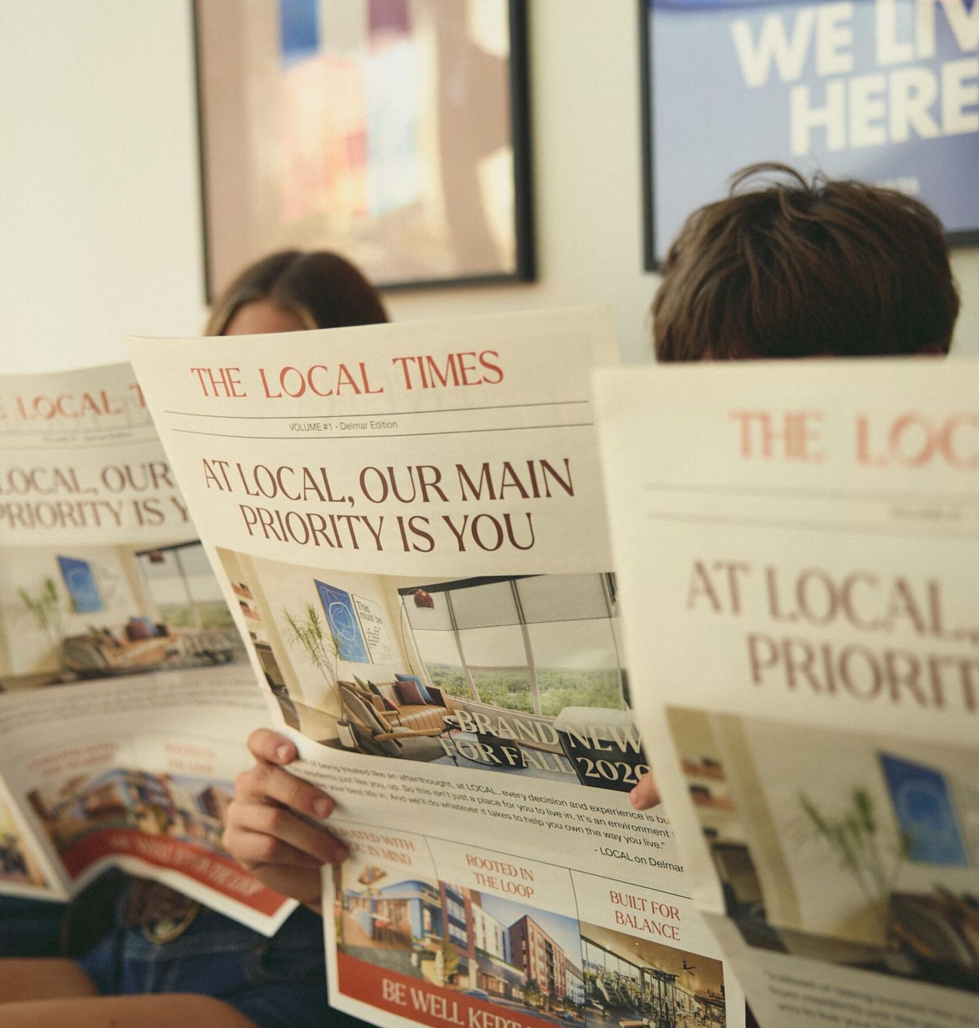 Two people sitting and reading newspapers titled "The Local Times" with headlines about local priorities.