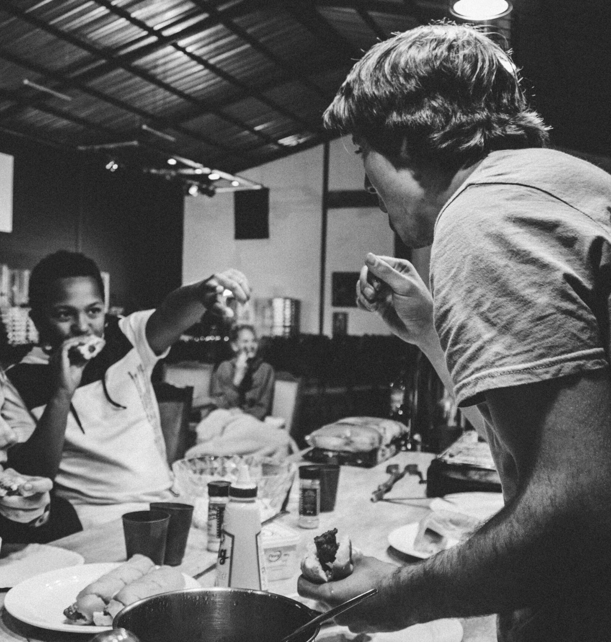 Four people enjoy eating together at a table, smiling and laughing in a casual indoor setting.