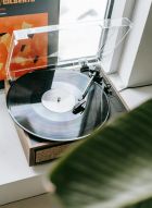 A vinyl record player plays a record by a window, with an album cover visible in the background.