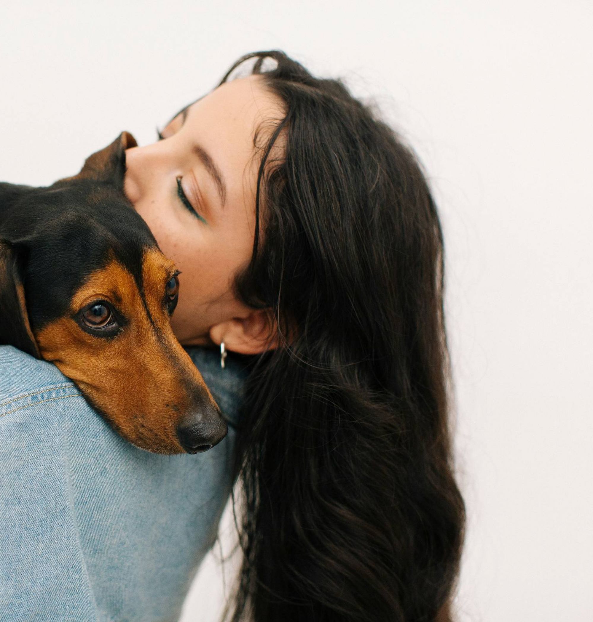Woman with long dark hair hugs a small brown and black dog, both appearing calm and affectionate.
