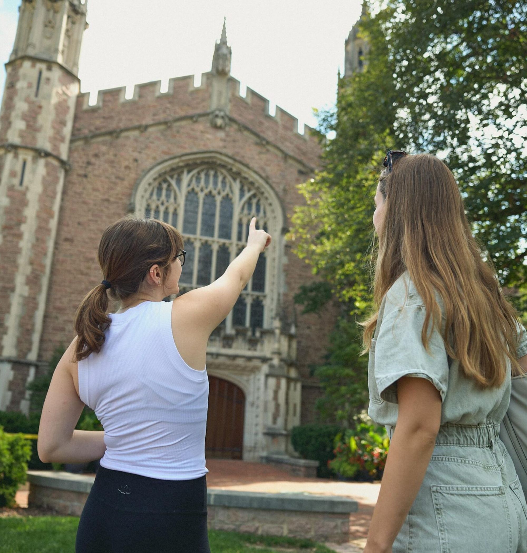 LOCAL On Delmar two women stand outside and admire a large, historic stone building with arched windows and greenery.