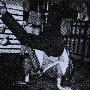 A person breakdancing on their head while another person crouches nearby, taking a photo.