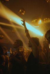 People dancing and raising drinks under golden lights at a lively, crowded nightclub or party.