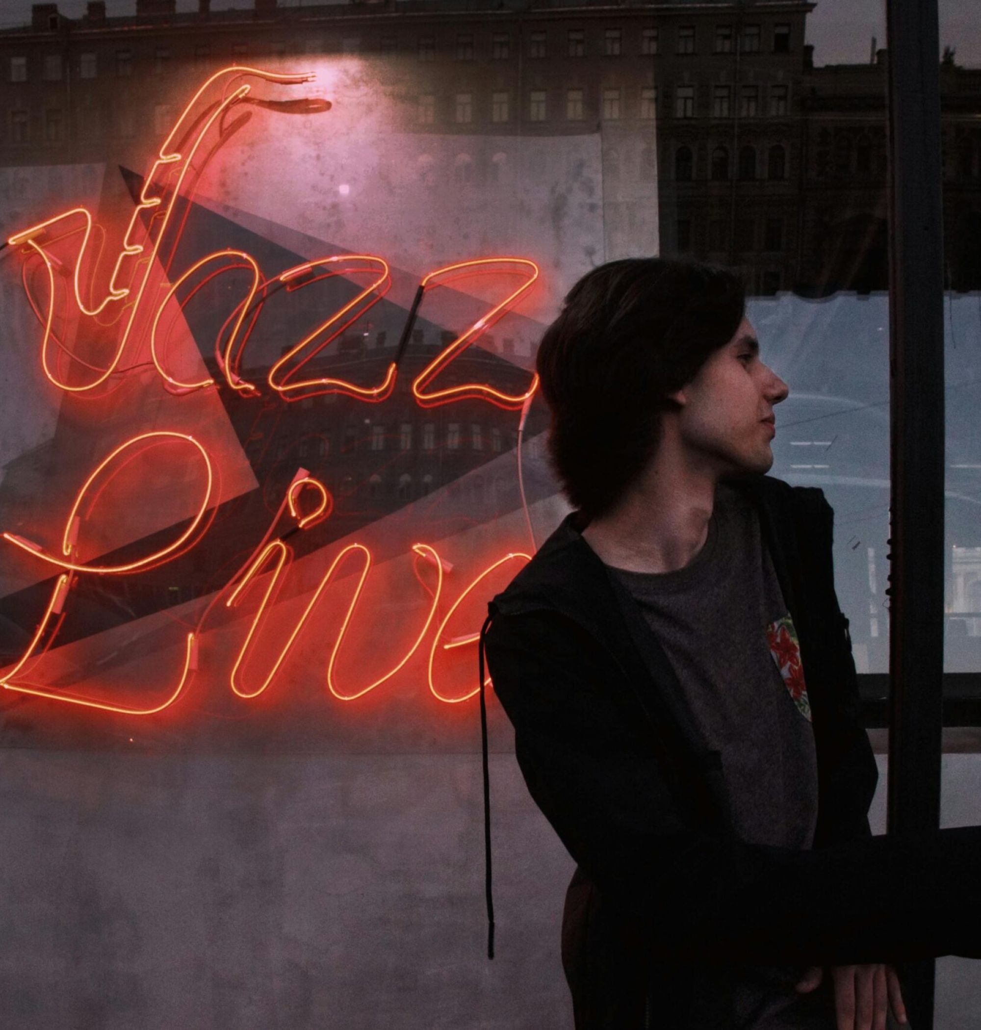 A person stands in front of a neon "Jazz Live" sign at dusk.