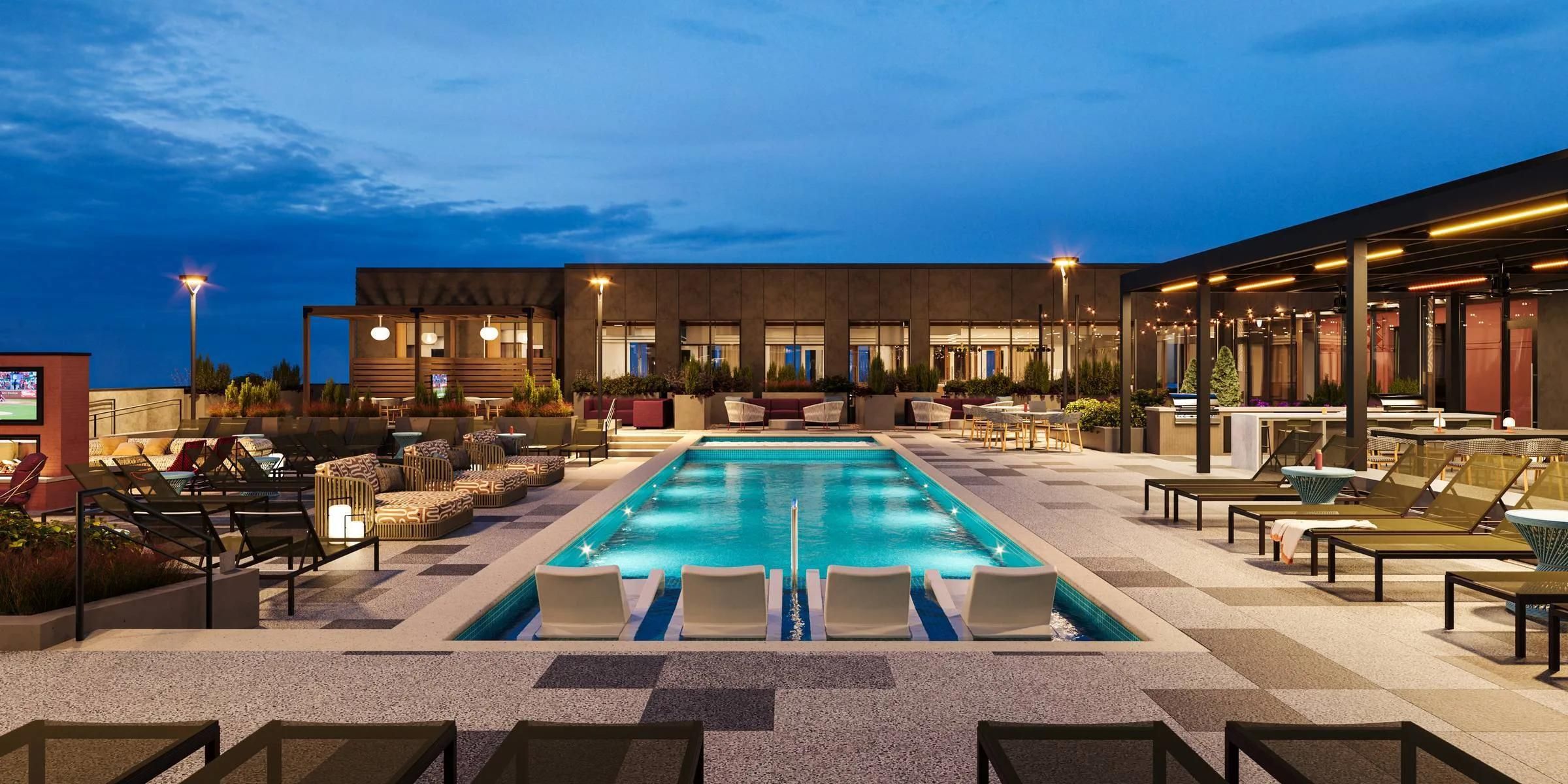 Rooftop pool with lounge chairs, outdoor seating, and modern lighting at sunset under a blue sky.