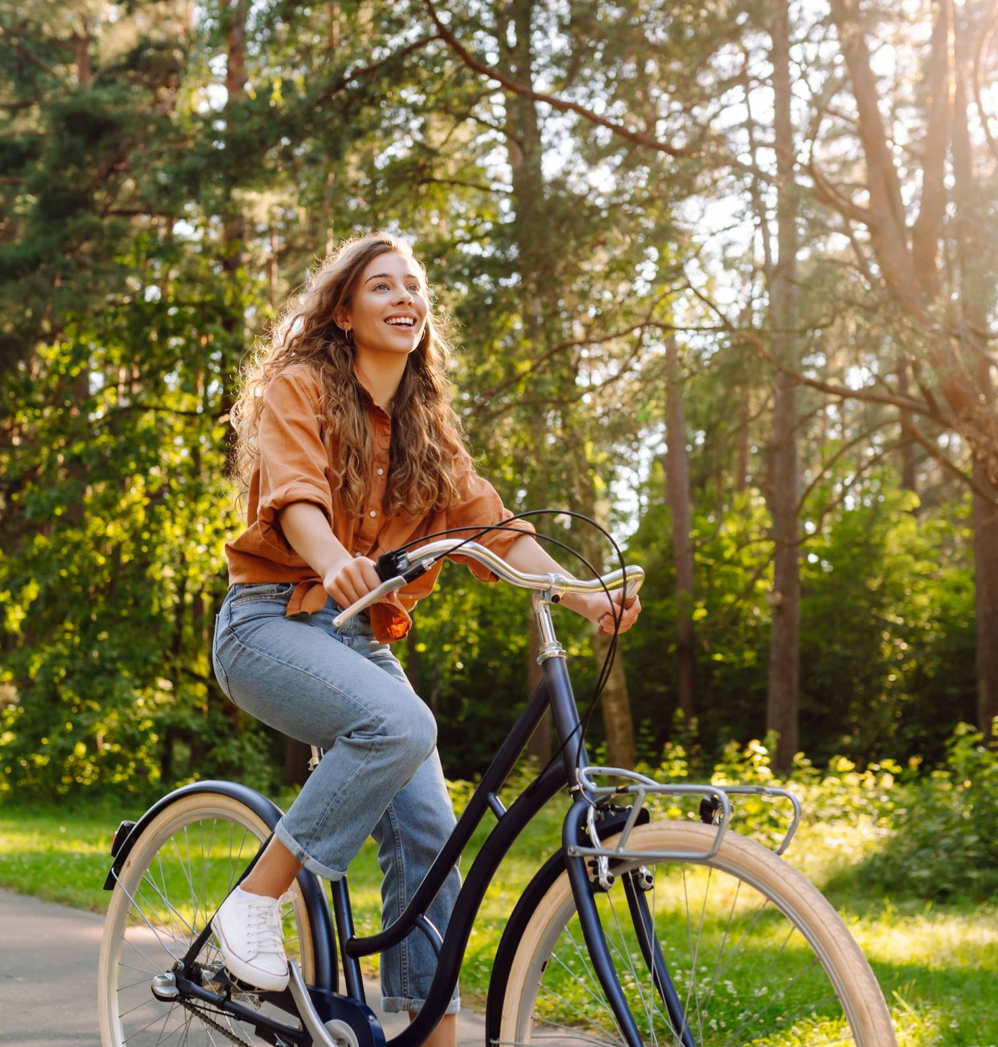 Young woman riding a bicycle on a sunny path in a forest, smiling and enjoying the outdoors.