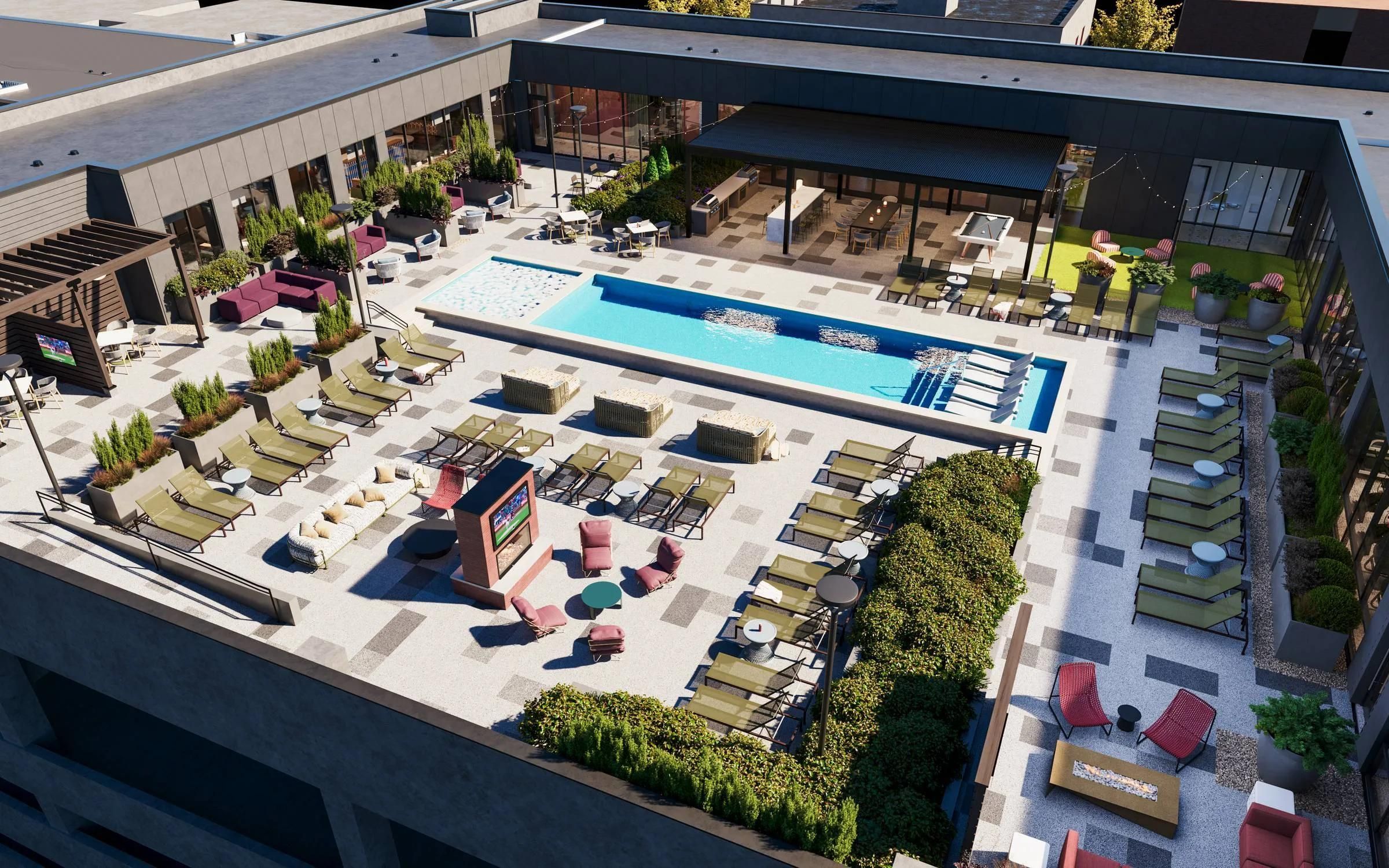 A rooftop pool area with lounge chairs, tables, greenery, and seating areas, viewed from above.