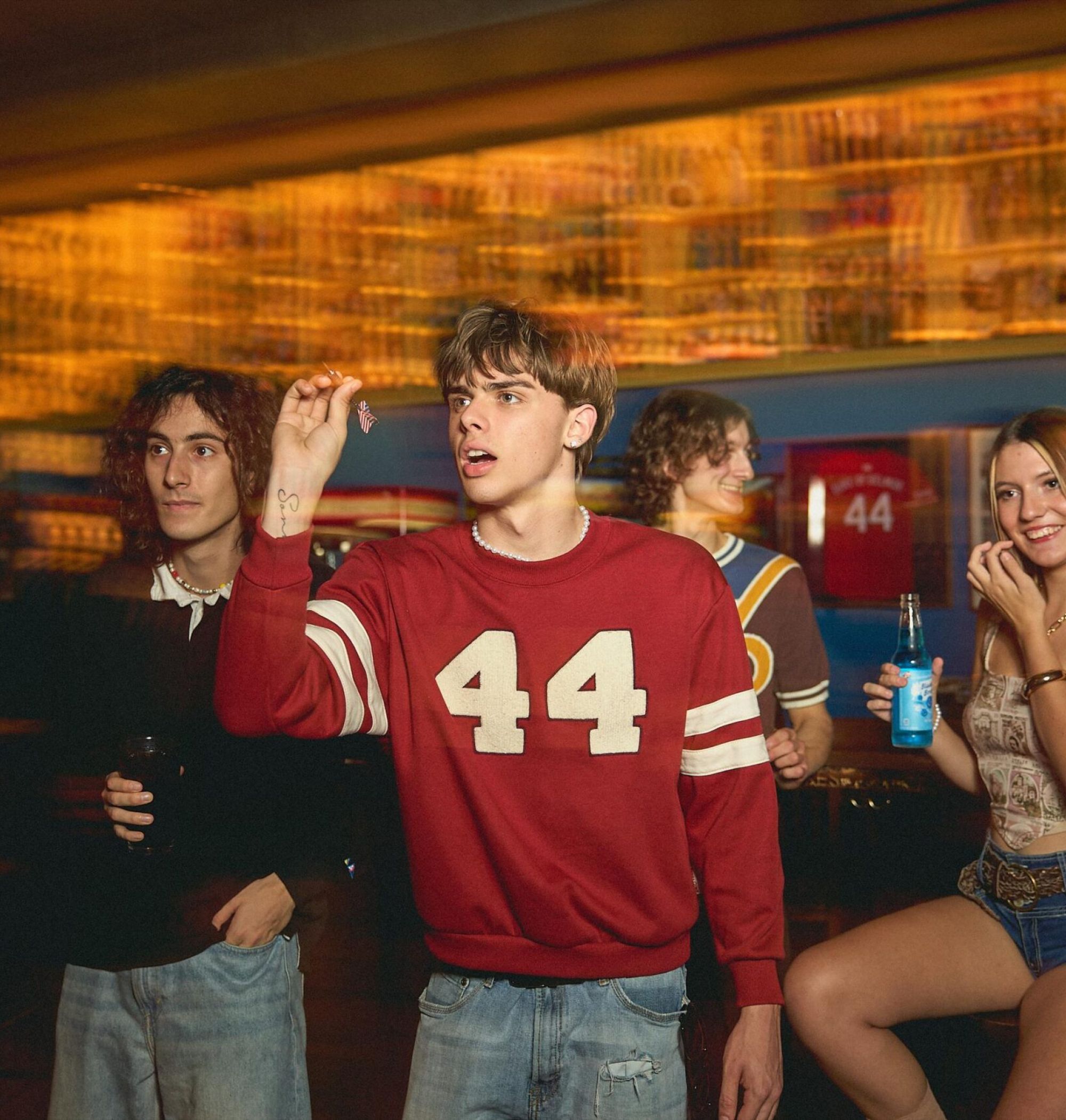 A group of young adults play darts and socialize in a lively bar or game room.