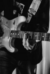 Black and white photo of a person playing an electric guitar, focused on their hand and guitar neck.