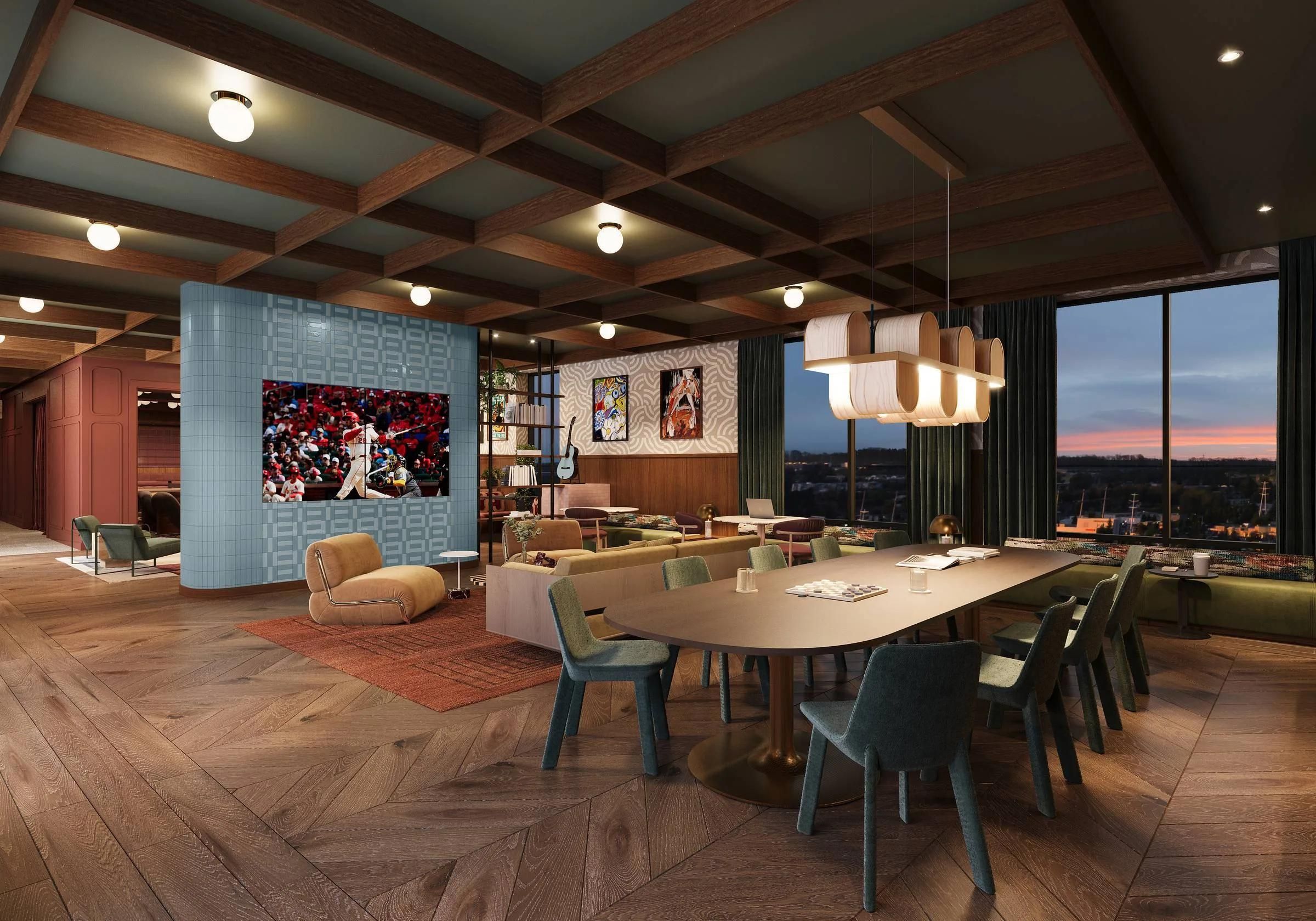 Modern lounge with a long dining table, cozy seating, TV on tiled wall, large windows, and sunset view.