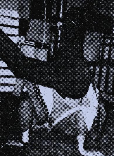 A person breakdancing on their head while another person crouches nearby, taking a photo.