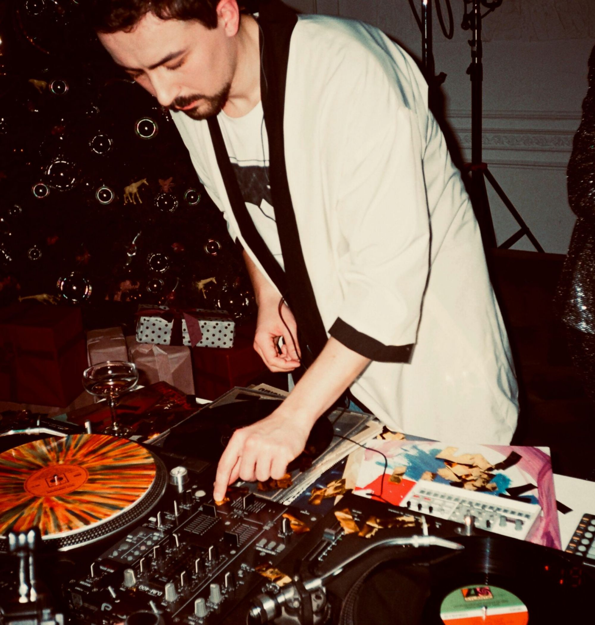 A DJ is mixing music on turntables at a lively indoor event with festive decorations.